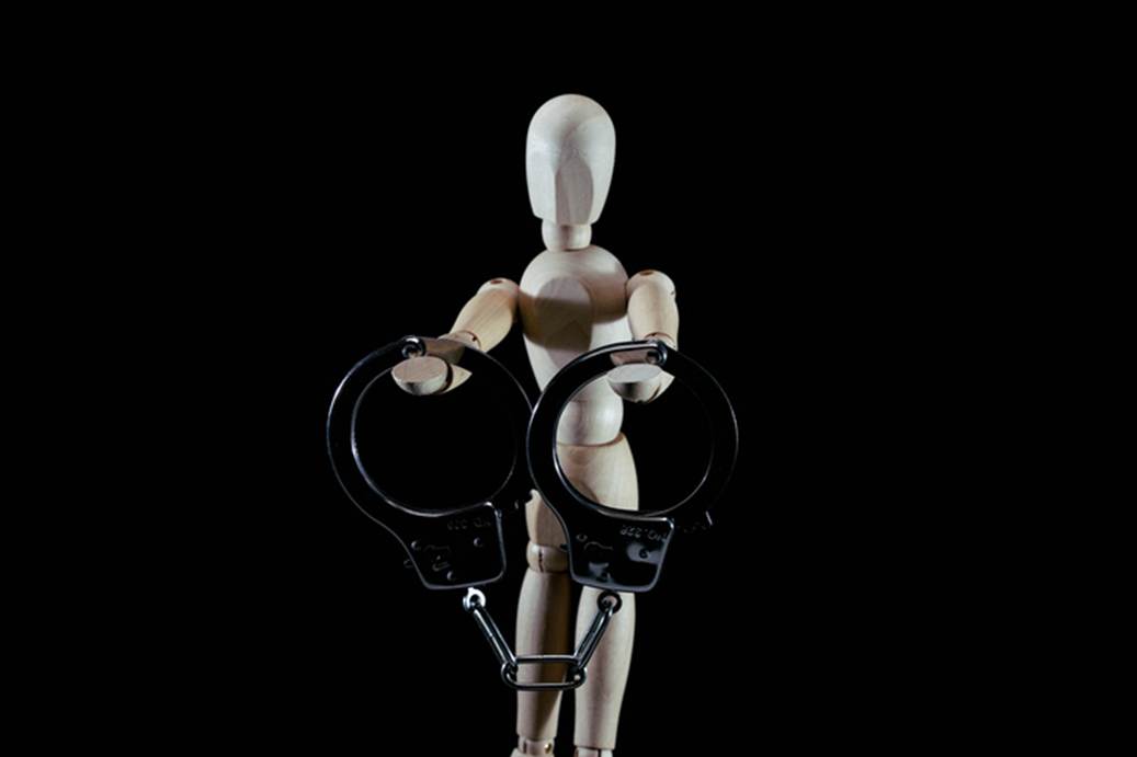 A wooden mannequin figure presents metal handcuffs against a stark black backdrop. The image relates to a section on the probable cause defense in legal cases.